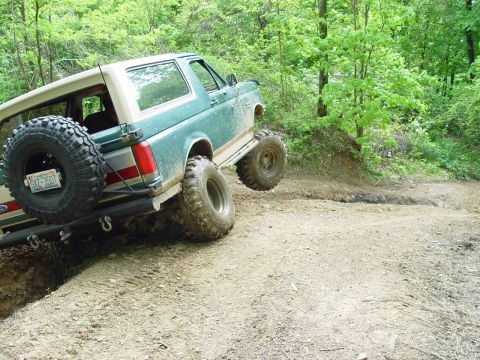 1996 Ford Bronco - A green Ford Bronco navigates a dirt trail with one wheel lifted off the ground.