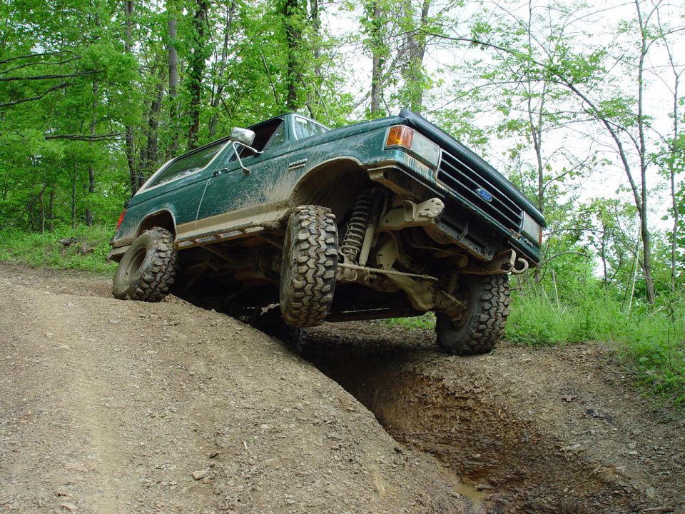 Lifted green two-tone Ford Bronco flexing over a dirt trail rut with front wheel lifted