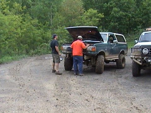 1996 Ford Bronco - Two men inspect a green Ford Bronco with its hood up, parked on a dirt road next to another vehicle.