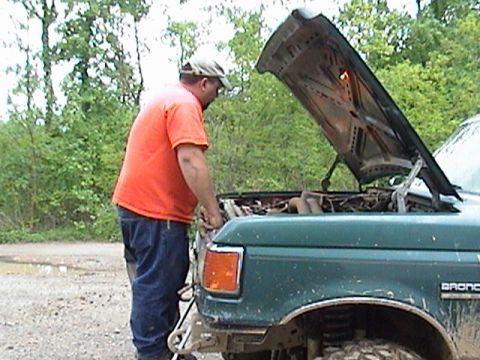 1996 Ford Bronco - A man works on the engine of a green 1996 Ford Bronco with its hood raised.