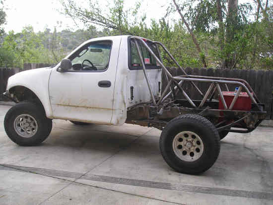 White 2002 Ford F-150 pickup truck, modified with a roll cage and fuel cell, viewed from the side