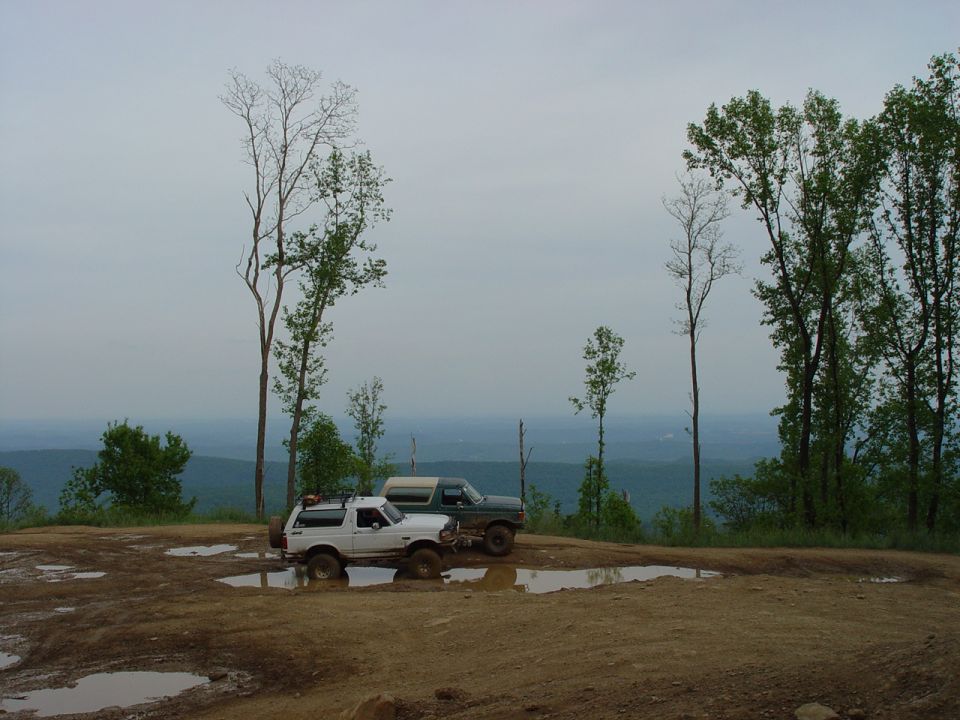 White 1996 Ford Bronco parked on muddy terrain with a second SUV behind it