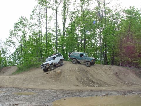1996 Ford Bronco - Two Ford Broncos navigate an off-road course on a dirt hill.