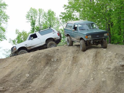 1996 Ford Bronco - Two Ford Broncos navigate a steep, muddy incline on an off-road trail.