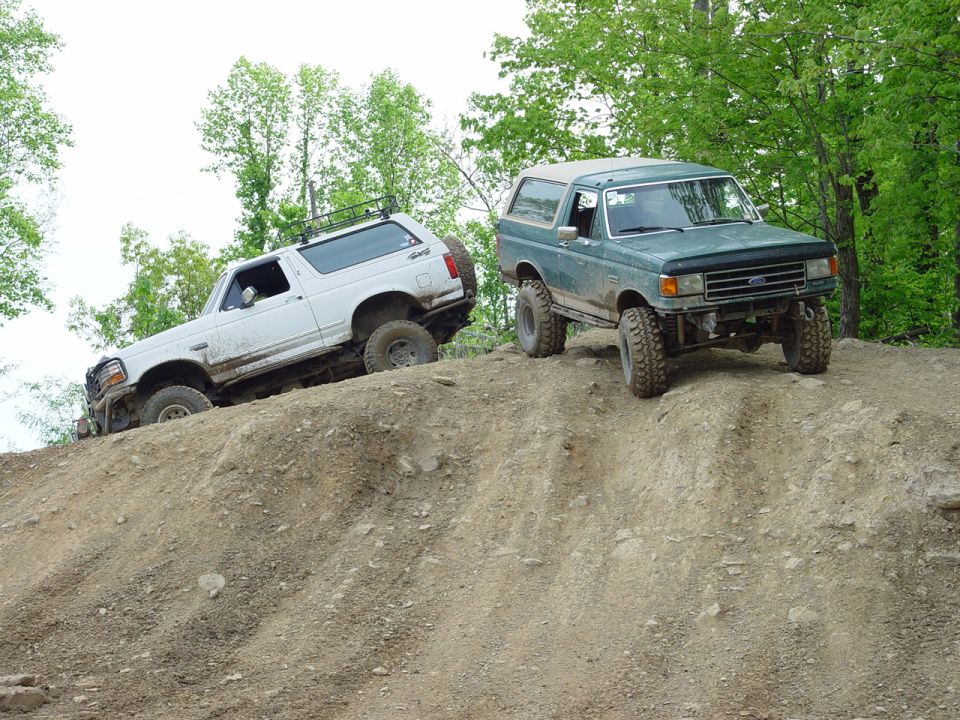 White Bronco climbing a dirt hill, green Bronco behind it