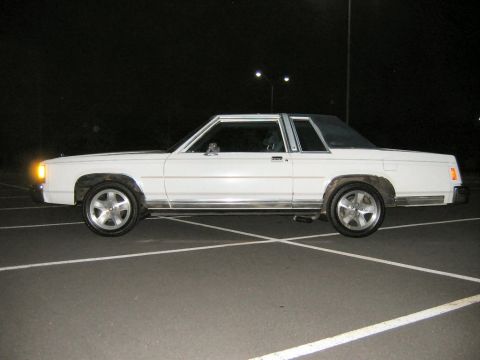 1985 Ford LTD Crown Victoria - White two-door Ford full-size coupe shown in left-side profile at night in an empty asphalt parking lot, with aftermarket multi-spoke alloy…