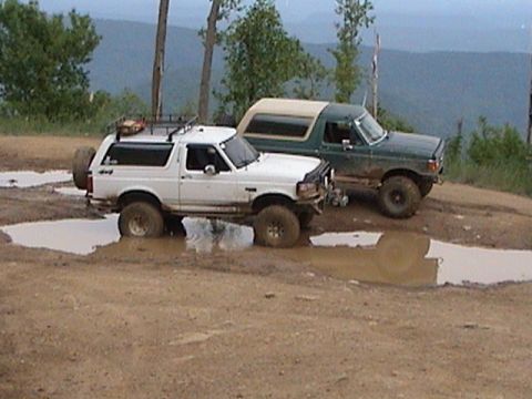 1996 Ford Bronco - Two Ford Broncos navigate muddy terrain, their off-road capabilities.
