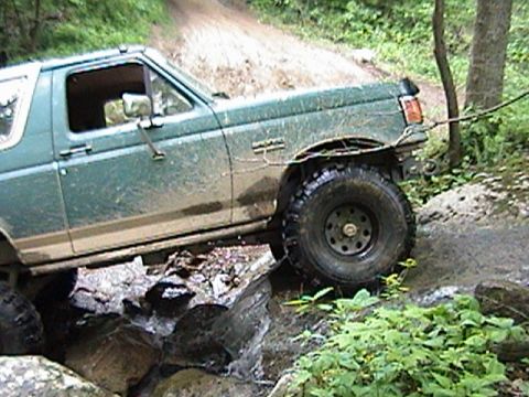 1996 Ford Bronco - Ford Bronco navigates a challenging off-road course with large rocks and water.