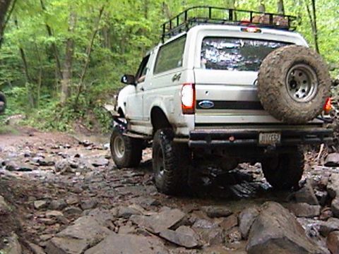 1996 Ford Bronco - This SUV is navigating a rocky trail, with a spare tire mounted on the rear and a roof rack.