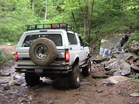 1996 Ford Bronco - A white Ford Bronco navigates a challenging off-road path with a stream and rocks.