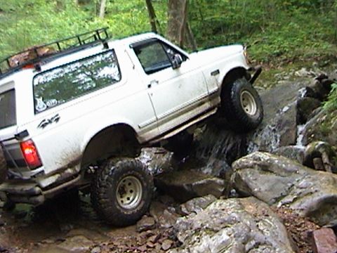 1996 Ford Bronco - White 1996 Ford Bronco climbs over rocks in a stream, demonstrating off-road capability.