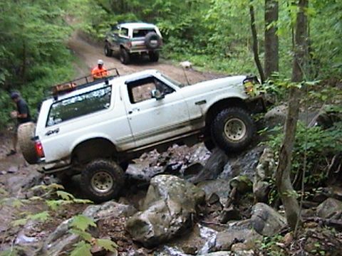 1996 Ford Bronco - Two Ford Broncos tackle a challenging off-road trail with steep, rocky inclines and muddy patches.