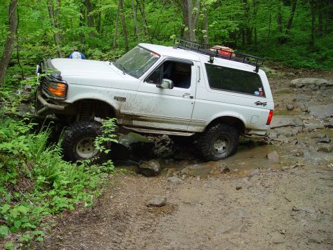 1996 Ford Bronco - White 1996 Ford Bronco tackling a challenging off-road course through mud and rocks.