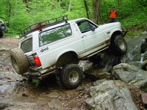 1996 Ford Bronco - A white Ford Bronco navigates a rocky stream, with another vehicle visible in the background.