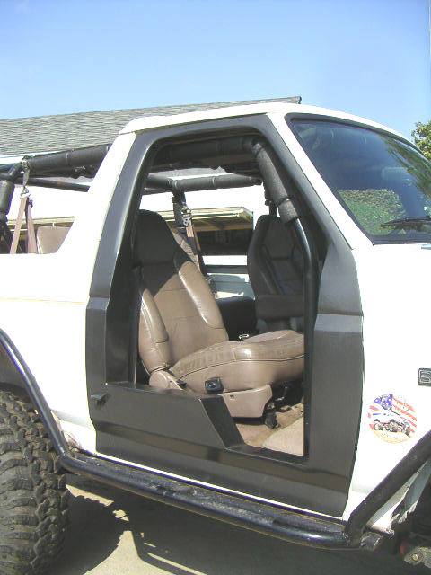 1996 Ford Bronco - The interior of a modified Ford Bronco is visible with the doors off, revealing the tan seats and roll cage structure.