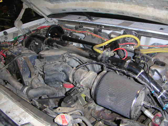 Ford truck engine bay with black cone air filter on custom intake tube and yellow wiring