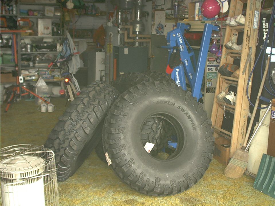 Three large Super Swamper tires in a garage, one with a white tag
