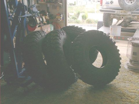 1978 Ford Bronco - Stack of off-road tires in a garage, with a trailer hitch and part of a vehicle in the background.