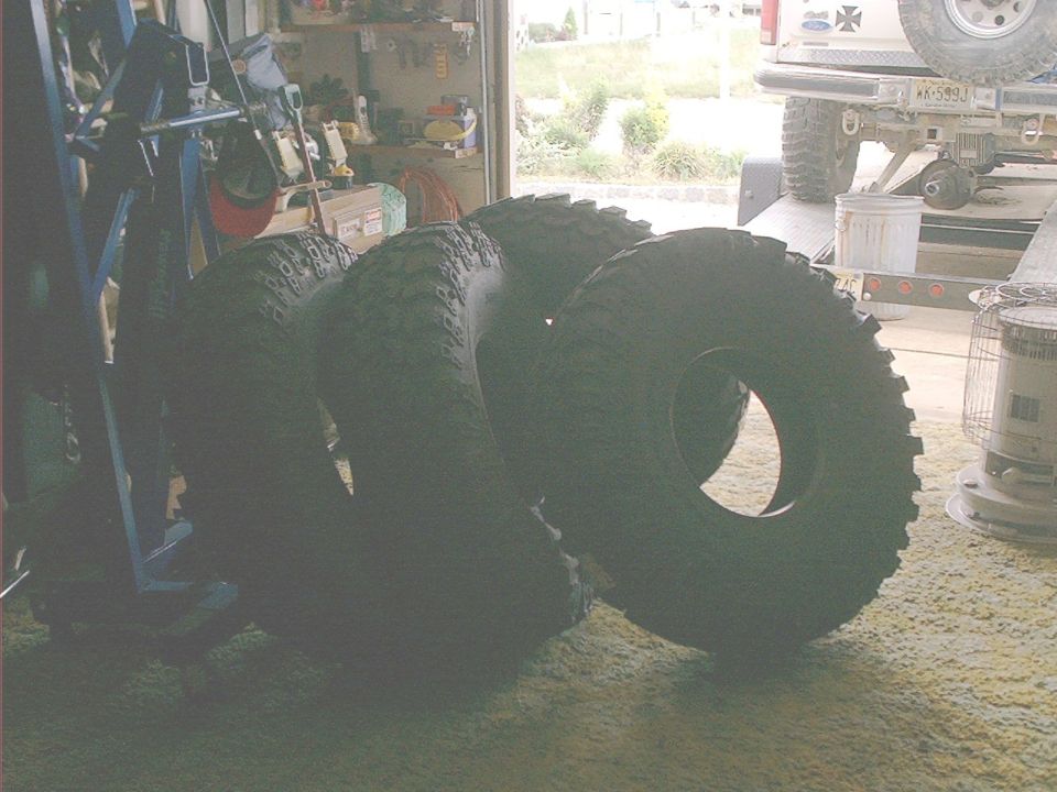 Several large off-road tires stacked on a garage floor, with a trailer hitch visible in the background