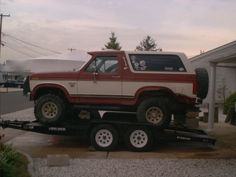 1986 Ford Bronco - A two-tone Ford Bronco is loaded onto a trailer, viewed from the side.