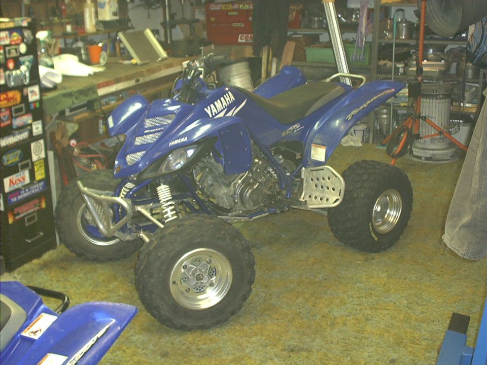 Blue Yamaha Raptor sport ATV parked in cluttered garage, 3/4 front view