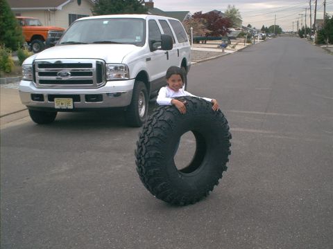 1978 Ford Bronco - A white Ford Excursion SUV is parked on a residential street, with a young girl posing behind a large tire.