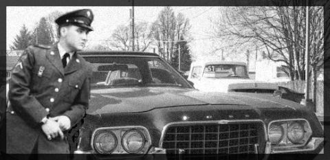 2002 Ford Crown Victoria - A man in a military uniform stands beside a dark-colored car, with a white truck visible in the background.