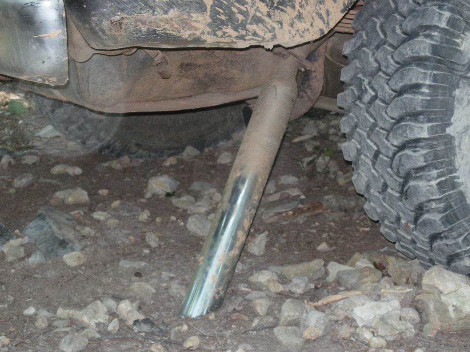 Chrome angle-cut exhaust tip exiting under a muddy truck beside a mud-terrain tire