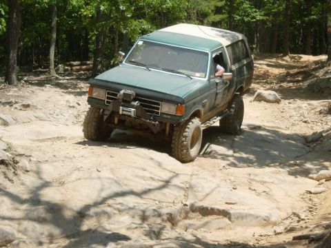 1995 Ford Bronco - Ford Bronco navigates a challenging rocky trail in a wooded area.