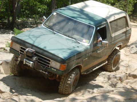 1995 Ford Bronco - This Ford Bronco is tackling a challenging off-road trail with large rocks and uneven ground.