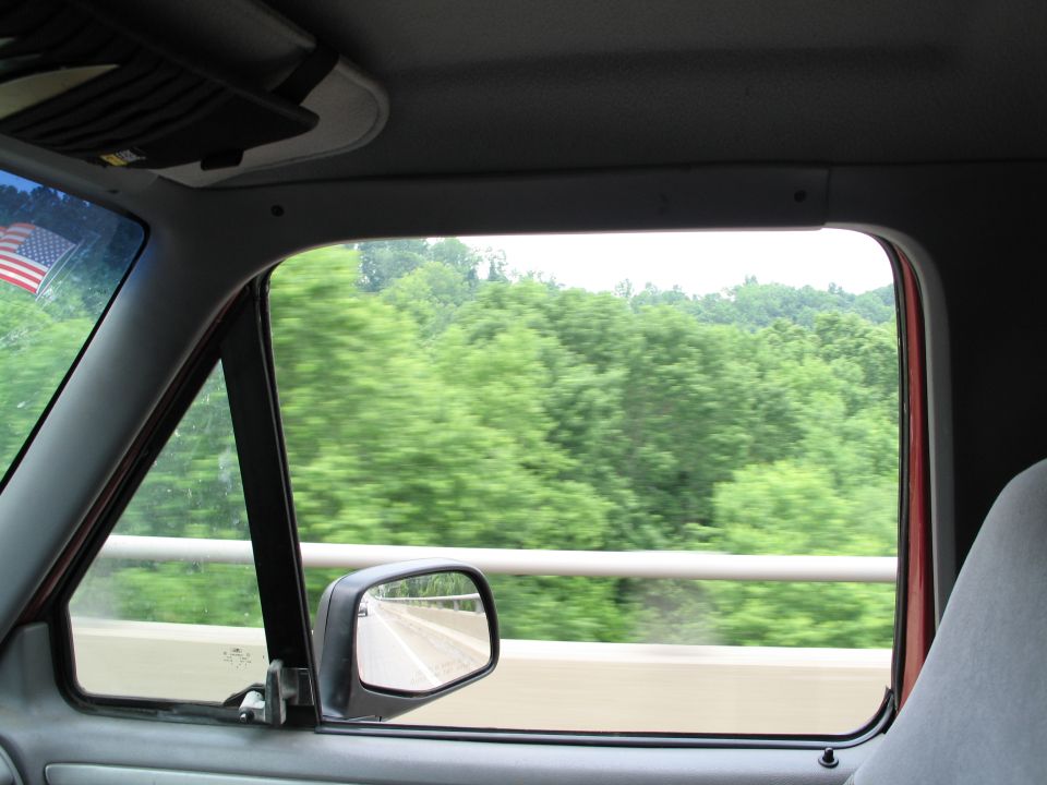 Interior view from passenger side window showing trees and a highway guardrail