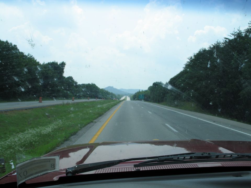 View from inside a vehicle driving on a highway with trees and hills in the distance