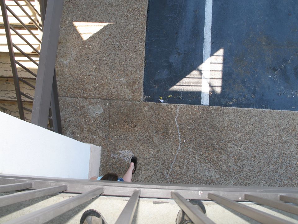 person lying on ground near parking lot, shadow of fence on pavement