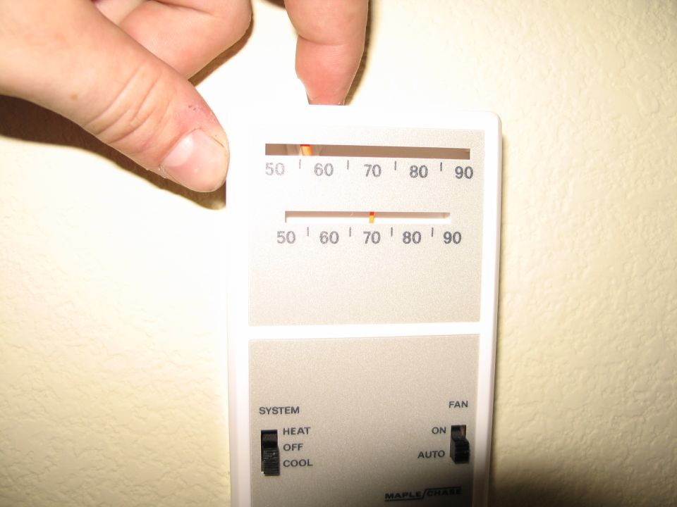 Hand adjusting a Maple Chase mechanical wall thermostat with slider scales