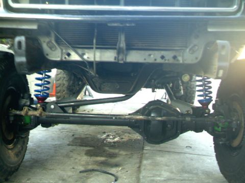 1989 Ford Bronco - The front suspension and axle of a modified off-road vehicle are shown, with blue coilover shocks visible.