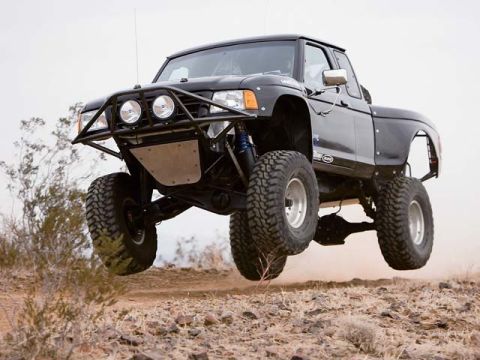 1984 Ford Bronco - This modified truck is captured mid-air, its off-road capabilities in a dusty, arid environment.