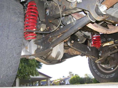 1984 Ford Bronco - Close-up view of the suspension system, red coil springs and a tire, with visible text on the tire.