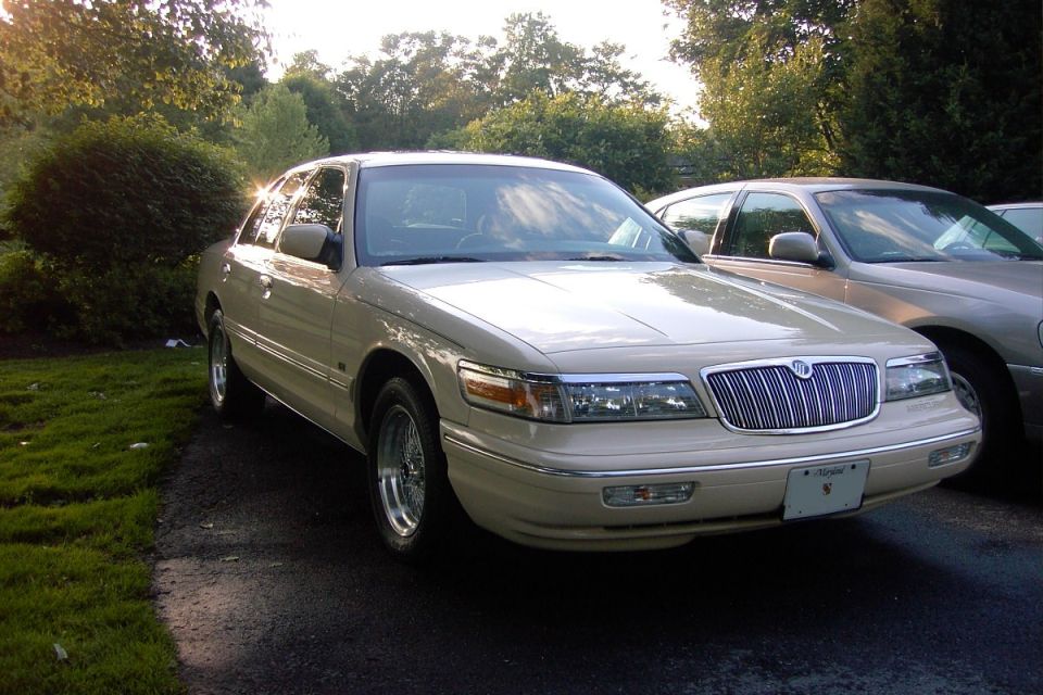 Cream Mercury Grand Marquis sedan, front 3/4 view, chrome grille and wire wheels, parked outdoors.