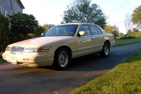 1996 Mercury Grand Marquis - A tan 1996 Mercury Grand Marquis sedan is parked on a driveway with grass and trees in the background.