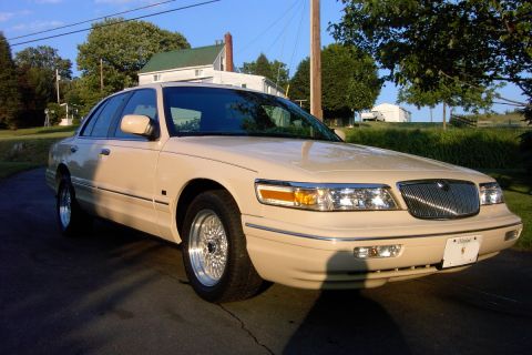 1996 Mercury Grand Marquis - A tan sedan is parked on a paved surface with a house and trees in the background.
