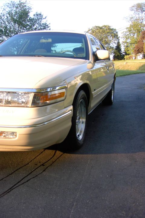 1996 Mercury Grand Marquis - A tan sedan is viewed from the front quarter angle, parked on an asphalt surface with trees in the background.