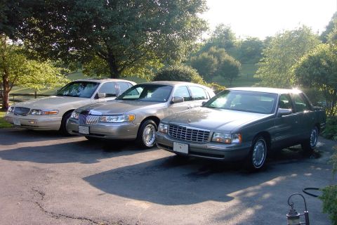 1996 Mercury Grand Marquis - Three luxury sedans are parked side-by-side on a paved surface with trees in the background.