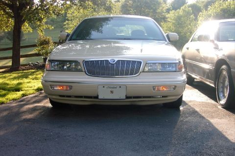 1996 Mercury Grand Marquis - A beige Mercury Grand Marquis is parked in a driveway with trees and grass in the background.