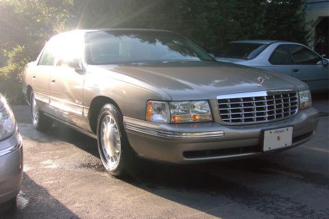 1996 Mercury Grand Marquis - A tan Cadillac sedan is parked on a wet asphalt surface, with another vehicle partially visible on the left.