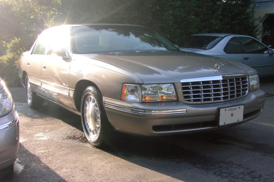 Tan Cadillac DeVille sedan, front 3/4 view, in sunlit driveway