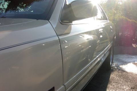 1996 Mercury Grand Marquis - A silver sedan's side profile is captured in bright sunlight, highlighting its chrome accents and subtle pinstripes.
