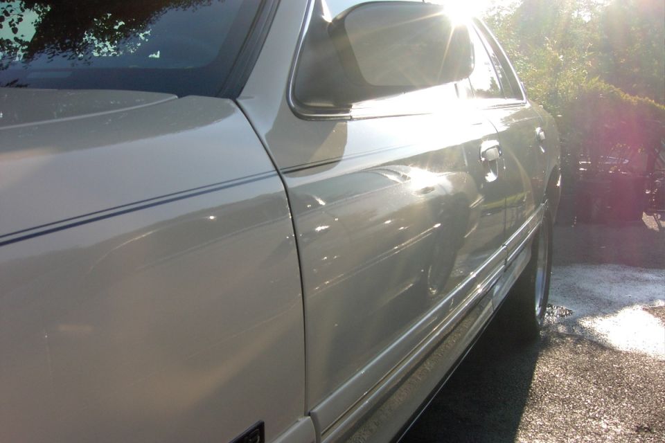 Cream sedan passenger side door and mirror in bright backlit sunlight