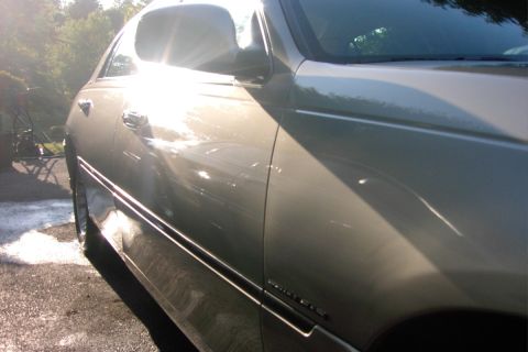 1996 Mercury Grand Marquis - A silver sedan is captured from the side, reflecting the bright sunlight on its polished surface.