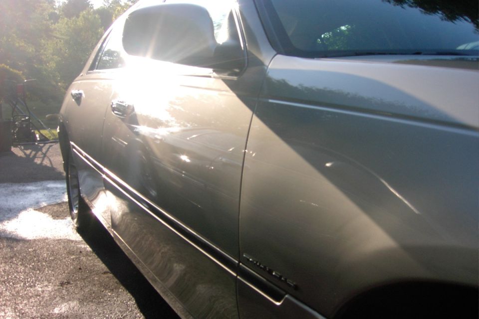 Sunlight flaring off the polished side of a champagne-gold sedan after a wash