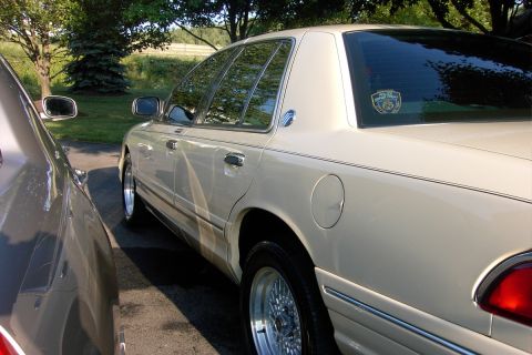 1996 Mercury Grand Marquis - A beige 1996 Mercury Grand Marquis sedan is parked next to another vehicle, with a police department sticker visible on the rear window.